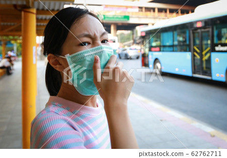 Tired asian child girl cough wearing hygienic mask,stressed worried about air pollution problems,toxic fumes,PM 2.5,dust,bad environment at bus stop in city,protect their health from pollution smog Tired asian child girl cough wearing hygienic mask,stressed worried about air pollution problems,toxic fumes,PM 2.5,dust,bad environment at bus stop in city,protect their health from pollution smog 62762711