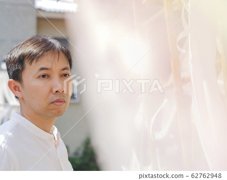 Happy Thai asian smart man wear casual white shirt is peeking back the white soft lace fabric curtain on sunshine, relaxing timesummer day. Asia Lifestyle chill out at outdoor.  He looking for someone 62762948