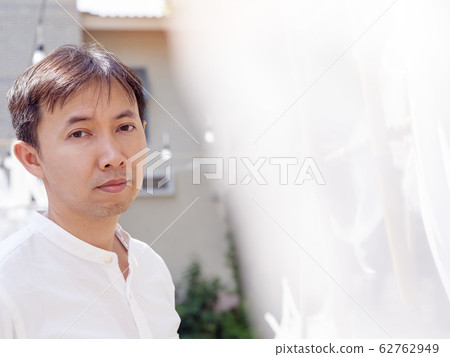 Happy Thai asian smart man wear casual white shirt is thinking, peeking back white soft lace fabric curtain on sunshine in relaxing time summer.  Asia Lifestyle chill out at outdoor.  Look at camera. 62762949