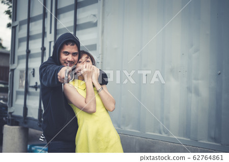 The bandit locks the woman's neck by his arm for a hostage and pointing knife forward. he wear black clothes. The bandit locks the woman's neck by his arm for a hostage and pointing knife forward. he wear black clothes. 62764861