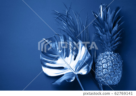 Painted exotic fruits, tropical palm, monstera leaves on classic blue background. Top view. Flat lay. Food concept. Creative layout of monochrome pineapple, banana, lemon with copy space. 62769141
