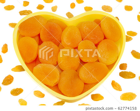 Heart shaped bowl of dried apricots isolated on white background with raisins Heart shaped bowl of dried apricots isolated on white background with raisins 62774158