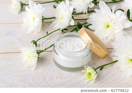 Moisturizing face cream in an open glass jar with golden lid and white chrysanthemum flowers Moisturizing face cream in an open glass jar with golden lid and white chrysanthemum flowers 62779822