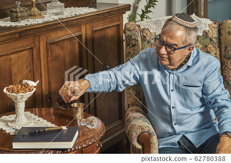 Senior Jew in armchair drinks wine in traditional home Senior Jew in armchair drinks wine in traditional home 62780388
