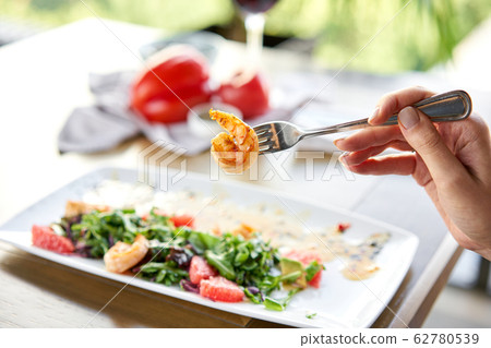 Closeup of grilled shrimps on a fork. Woman eats Delicious salad with slice grapefruit and arugula salad and spicy fried prawns. Restaurant menu, natural and organic food concept. 62780539
