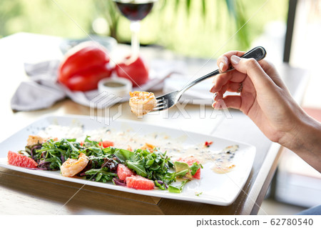 Closeup of grilled shrimps on a fork. Woman eats Delicious salad with slice grapefruit and arugula salad and spicy fried prawns. Restaurant menu, natural and organic food concept. 62780540