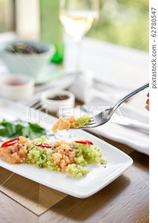 Closeup of salted and smoked salmon or trout fillet on a fork. Salmon tartare with cucumber and sesame seeds. Tasting dish on a wooden table. 62780547