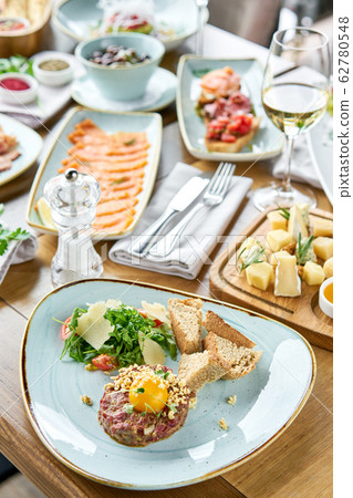 Beef tartar in the restaurant. Variety of dishes on the table. Various snacks and antipasti on the table. Restaurant menu. Italian cuisine 62780548