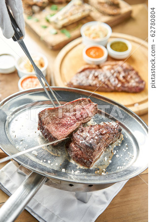 The waiter is butchering griled meat with a knife. Grilled fillet steaks with Pickled cabbage and two sauces.. Barbecue restaurant menu. 62780804