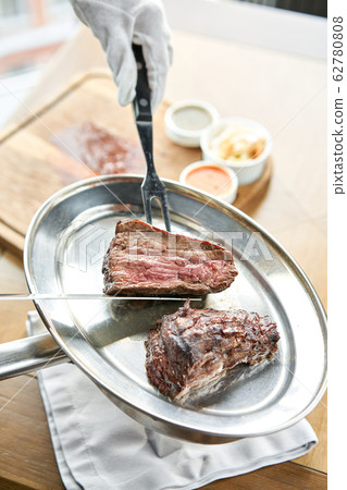 The waiter is butchering griled meat with a knife. Grilled fillet steaks with Pickled cabbage and two sauces.. Barbecue restaurant menu. The waiter is butchering griled meat with a knife. Grilled fillet steaks with Pickled cabbage and two sauces.. Barbecue restaurant menu. 62780808
