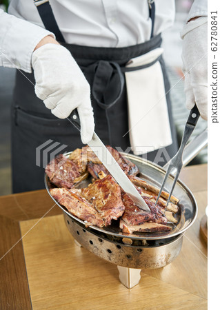 The waiter is butchering with a knife. Set of Various grilled meats . Barbecue restaurant menu, a series of photos of different meats. The waiter is butchering with a knife. Set of Various grilled meats . Barbecue restaurant menu, a series of photos of different meats. 62780841