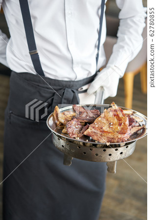 The waiter is holding a plate Various grilled meat set. Barbecue restaurant menu, a series of photos of different meats. The waiter is holding a plate Various grilled meat set. Barbecue restaurant menu, a series of photos of different meats. 62780855