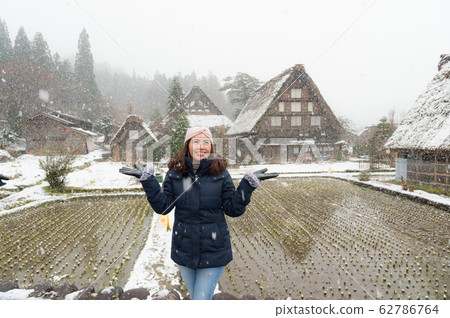 woman standing and holding transparent umbrella in the winter with background of snow is falling and covered throughout  ancient house at Shirakawa-go village at Gifu, Japan. 62786764