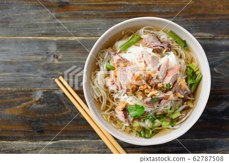 Rice noodles soup with beef in a bowl and chopsticks on wooden table, Asian food, Top view Rice noodles soup with beef in a bowl and chopsticks on wooden table, Asian food, Top view 62787508