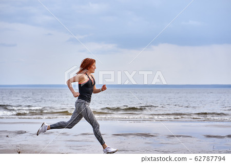 A red-haired middle-aged woman in sportswear runs A red-haired middle-aged woman in sportswear runs 62787794