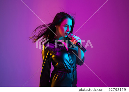 Caucasian female singer portrait isolated on purple studio background in neon light Caucasian female singer portrait isolated on purple studio background in neon light 62792159