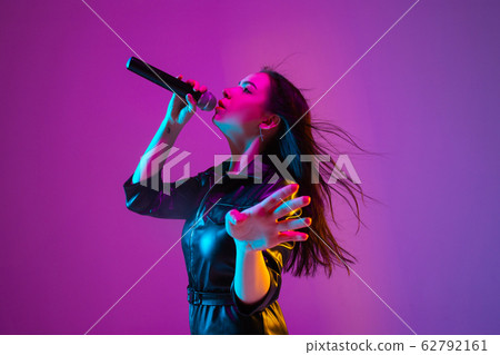Caucasian female singer portrait isolated on purple studio background in neon light 62792161