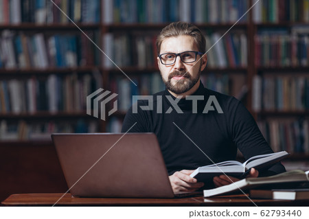 Bearded man sitting at library with books and laptop 62793440