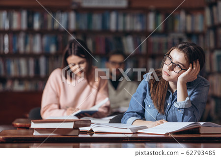 Pretty girl dreaming about party while studying at library Pretty girl dreaming about party while studying at library 62793485