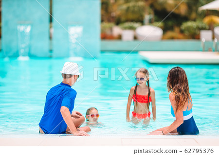 Happy family of four in outdoors swimming pool 62795376