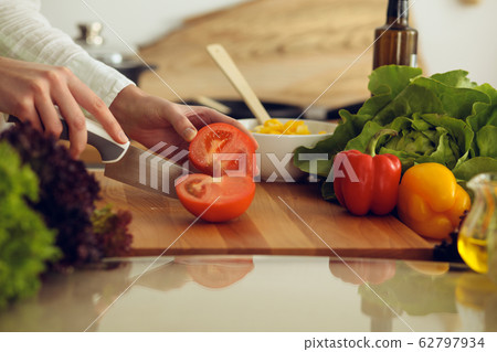 Unknown human hands cooking in kitchen. Woman slicing red tomatoes. Healthy meal, and vegetarian food concept Unknown human hands cooking in kitchen. Woman slicing red tomatoes. Healthy meal, and vegetarian food concept 62797934