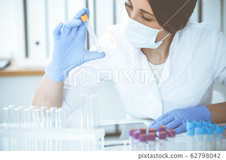 Close-up of professional female scientist in protective eyeglasses making experiment with reagents in laboratory. Medicine and research concept Close-up of professional female scientist in protective eyeglasses making experiment with reagents in laboratory. Medicine and research concept 62798042