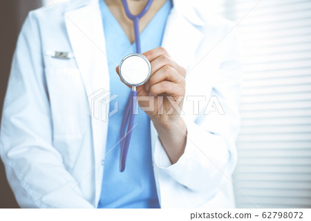 Unknown doctor woman holds stethoscope head, close-up. Physician ready to examine and help patient. Helping and insurance in health care, best treatment and medicine concept Unknown doctor woman holds stethoscope head, close-up. Physician ready to examine and help patient. Helping and insurance in health care, best treatment and medicine concept 62798072