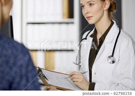 Cheerful smiling female doctor and patient woman discussing current health examination while sitting in clinic. Perfect medical service in hospital. Medicine concept 62798158