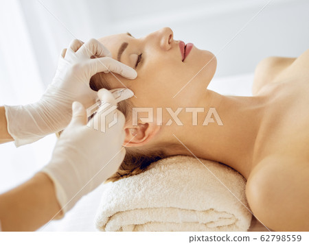 Beautiful woman receiving beauty injections with closed eyes. Beautician doctor hands doing beauty procedure to female face with syringe. Cosmetic medicine and surgery concept 62798559
