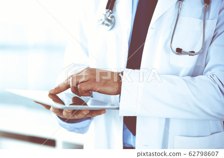 Doctor man using tablet computer for network research or virtual disease treatment, hands close-up. Perfect medical service in clinic. Modern medicine, medic data and healthcare concepts. Toned Doctor man using tablet computer for network research or virtual disease treatment, hands close-up. Perfect medical service in clinic. Modern medicine, medic data and healthcare concepts. Toned 62798607