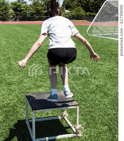 Young female athlete jumping on to a plyo box 62799080