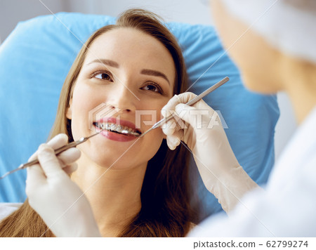 Smiling young woman with orthodontic brackets examined by dentist at dental clinic. Healthy teeth and medicine concept 62799274