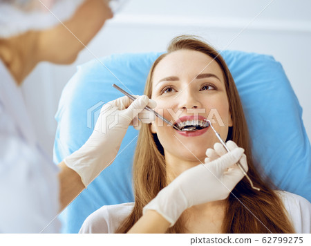 Smiling young woman with orthodontic brackets examined by dentist at dental clinic. Healthy teeth and medicine concept 62799275