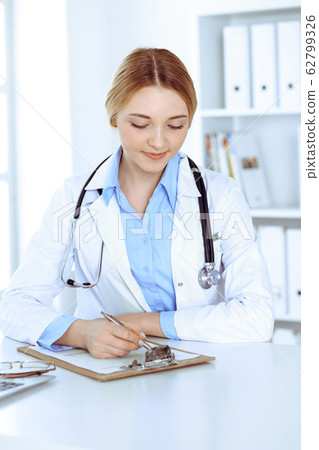 Young woman doctor at work while filling up medication history records in hospital office. Physician controls exam results. Medicine and healthcare concept 62799326