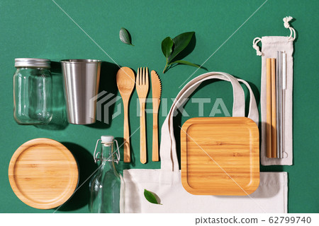 Cotton bags, glass jar, bottle, metal cup, straws for drinking, bamboo cutlery and boxes on green background. Sustainable lifestyle. Zero waste, plastic free shopping concept Cotton bags, glass jar, bottle, metal cup, straws for drinking, bamboo cutlery and boxes on green background. Sustainable lifestyle. Zero waste, plastic free shopping concept 62799740