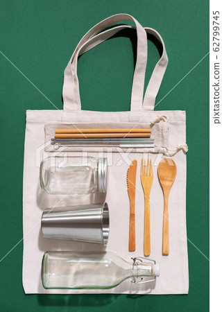 Sustainable lifestyle. Zero waste, plastic free shopping concept. Cotton bags, glass jar, bottle, metal cup, straws for drinking, bamboo cutlery and boxes on green background. 62799745