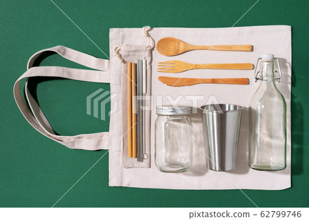 Cotton bags, glass jar, bottle, metal cup, straws for drinking, bamboo cutlery and boxes on green background. Sustainable lifestyle. Zero waste, plastic free shopping concept 62799746