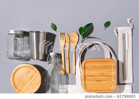 Sustainable lifestyle. Zero waste, plastic free shopping concept. Cotton bags, glass jar, bottle, metal cup, straws for drinking, bamboo cutlery and boxes on gray background. Sustainable lifestyle. Zero waste, plastic free shopping concept. Cotton bags, glass jar, bottle, metal cup, straws for drinking, bamboo cutlery and boxes on gray background. 62799805