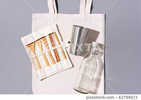 Cotton bags, glass bottle, metal cup, bamboo cutlery on gray background. Sustainable lifestyle. Zero waste, plastic free shopping concept. 62799815