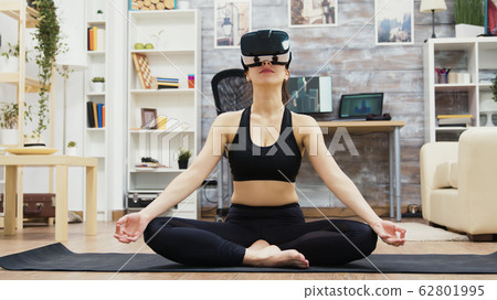 Beautiful young woman wearing virtual reality glasses doing yoga Beautiful young woman wearing virtual reality glasses doing yoga 62801995