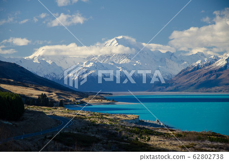 Snow covered Mount Cook with Lake Pukaki in the foreground and blue sky and white clouds, South Island, New Zealand Snow covered Mount Cook with Lake Pukaki in the foreground and blue sky and white clouds, South Island, New Zealand 62802738