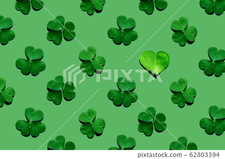 Pattern of shamrock leaves and one heart-shaped leaf on green background. Pattern of shamrock leaves and one heart-shaped leaf on green background. 62803394