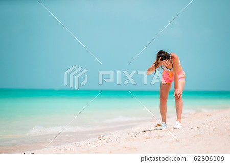 Fit young woman doing exercises on tropical white beach in her sportswear 62806109