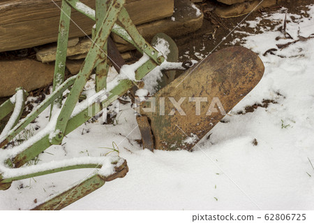 Old rusty plough in snow and wooden cabin 62806725