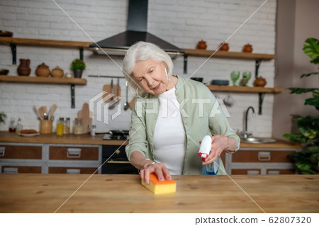 Elderly woman cleaning a table in her kitchen Elderly woman cleaning a table in her kitchen 62807320