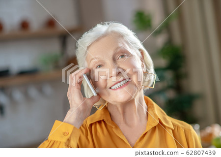 Cheerful elderly woman talking on the phone with her friend Cheerful elderly woman talking on the phone with her friend 62807439