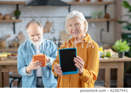 Stylish elderly woman showing her tablet in the blue case 62807441