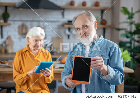 Handsome elderly man showing his tablet in a blue case Handsome elderly man showing his tablet in a blue case 62807442