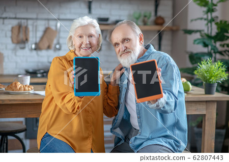 Elderly man and woman showing their tablets in colourful cases Elderly man and woman showing their tablets in colourful cases 62807443