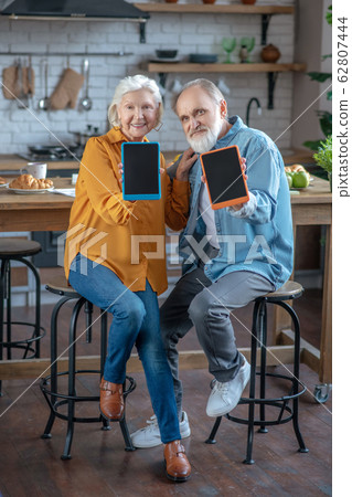 Cheerful couple of seniors showing their new tablets Cheerful couple of seniors showing their new tablets 62807444
